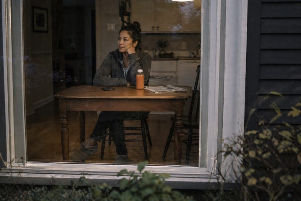 Woman sitting at a kitchen table at dusk with a bottle of orange juice during her second cleanse