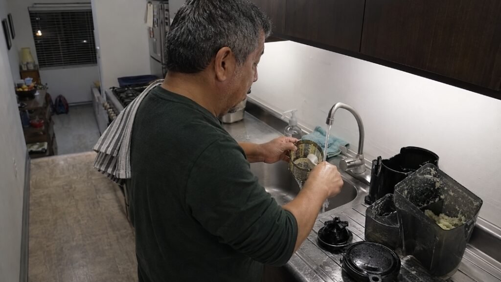 Man cleaning a juicer filter screen under running water after juicing
