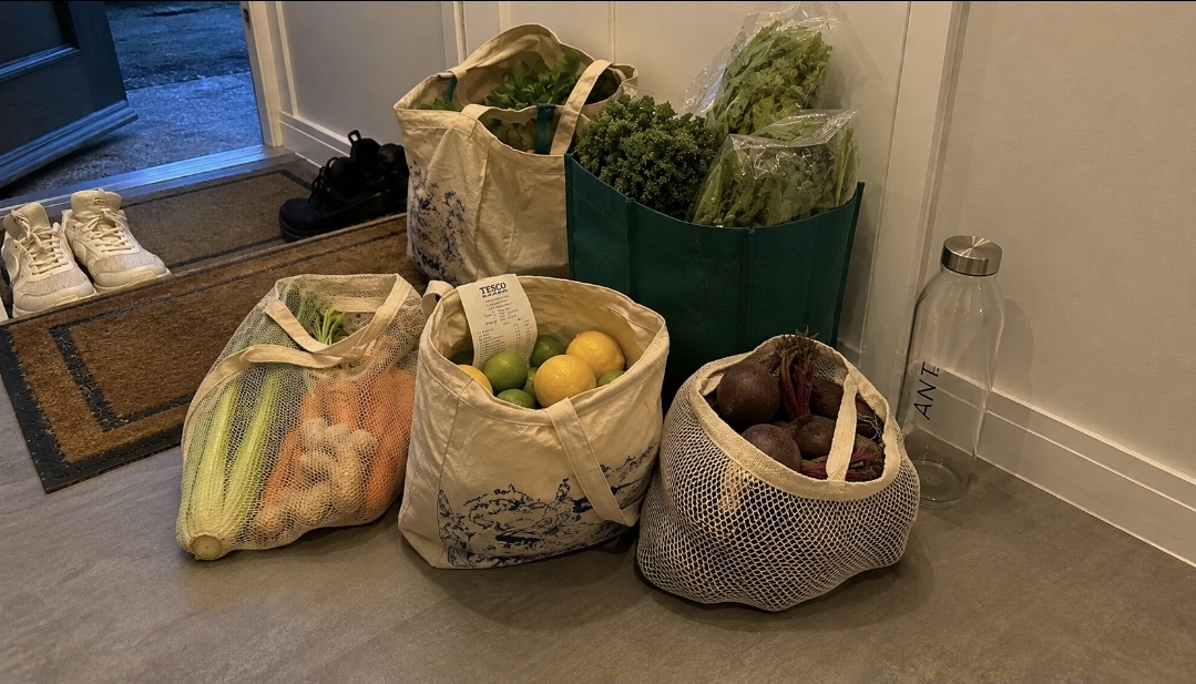 Juice Shop Unpacked Juice fast shopping bags unpacked by the front door with vegetables, herbs, citrus, ginger and an empty bottle